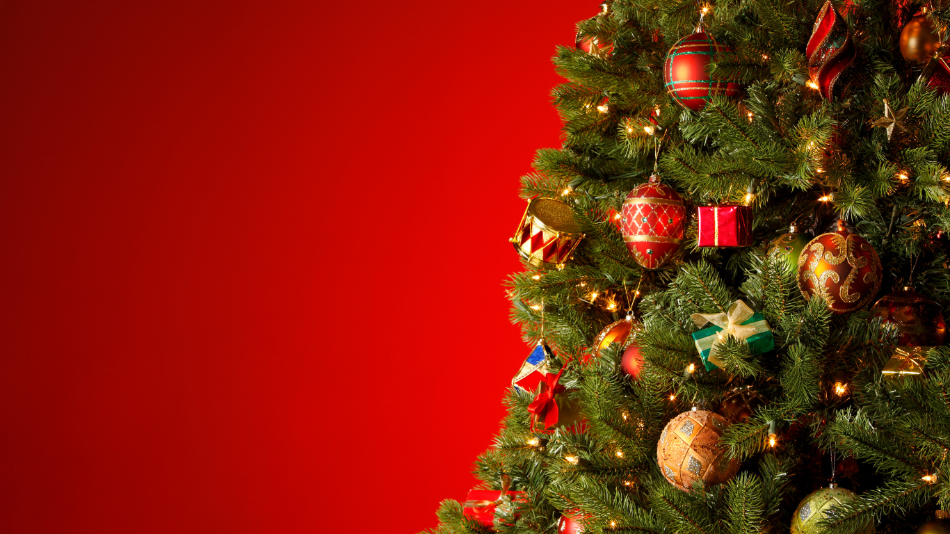 Een versierde kerstboom met kleurrijke ballen, linten en lichtjes staat tegen een rode achtergrond.